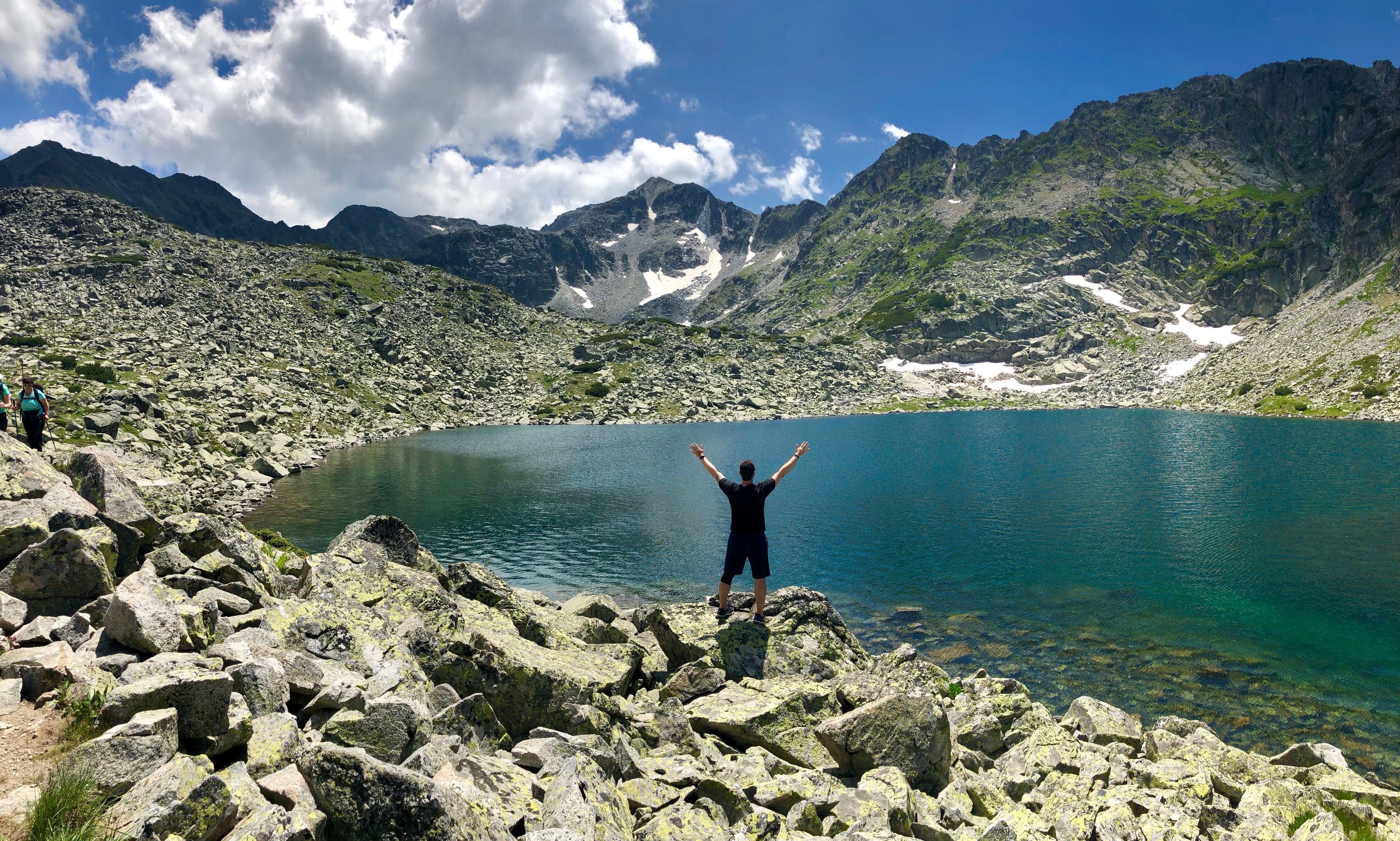Caption: A photo of Google Moderator @FelipePk with his hands raised and facing a clear-water lake in Rila National Park, Bulgaria, with Musala Peak in the background. (Local Guide @FelipePk)