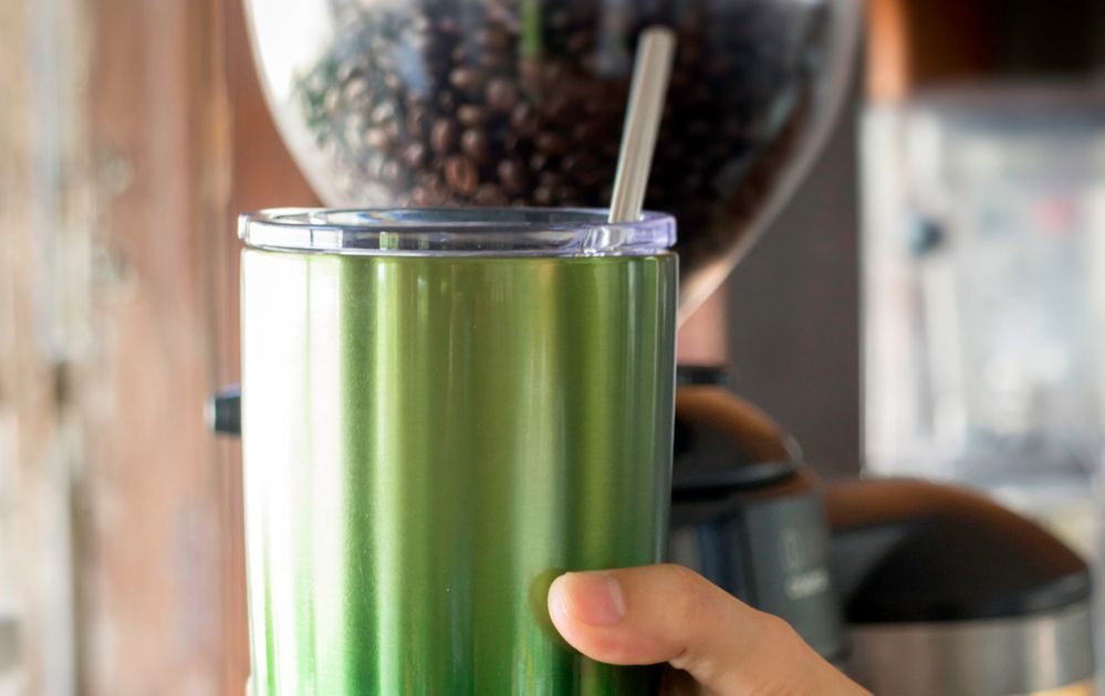 Caption: A photo of a green travel mug in a person’s hand at a coffee shop. (Getty Images)