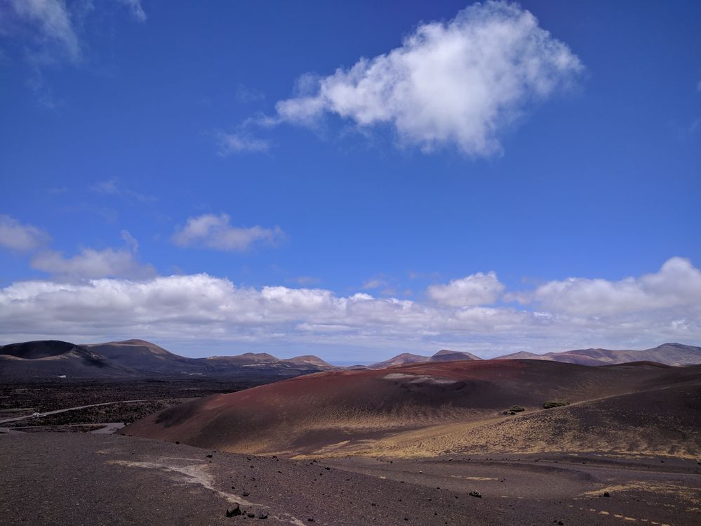 Caption: A photo of the landscape in Timanfaya National Park, Lanzarote, showing red soil hills and the volcano on the left. (Local Guide @MoniDi)