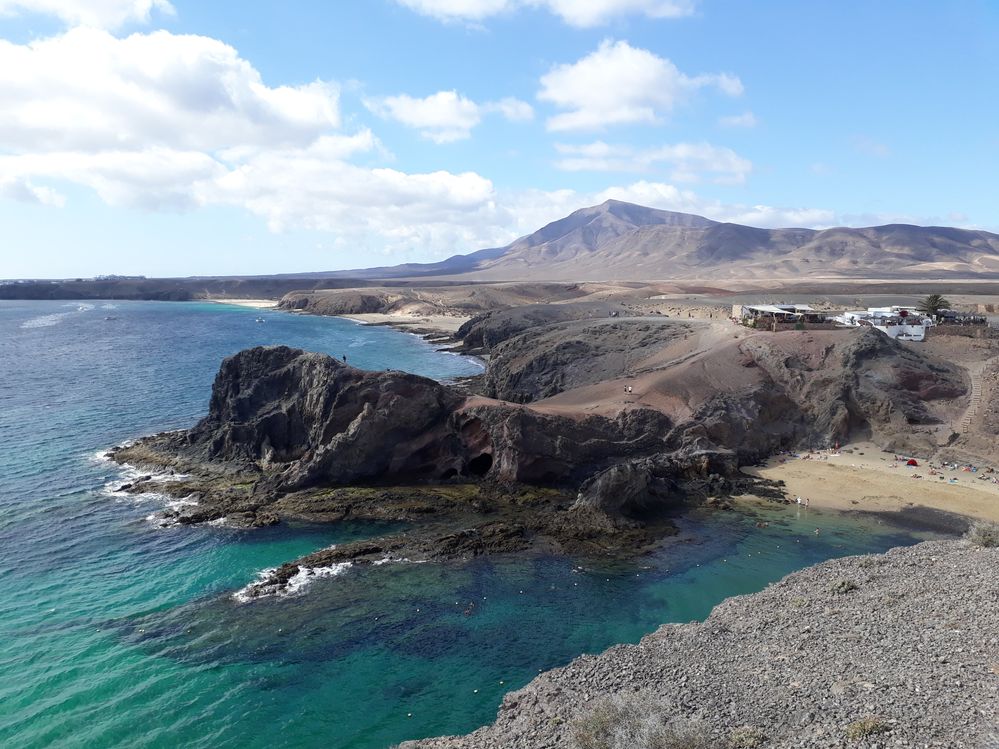 Caption: A photo of Papagayo Beach in Lanzarote, surrounded by cliffs and washed by emerald green sea waters. (Local Guide @MoniDi)