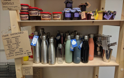 Shelves stocked with jars of preserves and sustainable and multiple-use drinking bottles, stainless steel straws